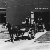 Image: Horse-drawn carts containing bags of sugar travel into a large corrugated metal-clad warehouse, while empty carts are transported out of another