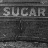 Image: A brick archway with the words ‘Glanville Sugar Refinery’ painted at its top is visible in front of a pile of burned, collapsed corrugated metal sheeting