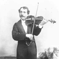 Image: A young moustachioed man in formal attire poses with a violin for a full-length photographic portrait