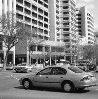 Image: late 1990s and early 2000s cars wait at an intersection of a street lined with skyscrapers