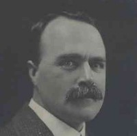 Image: A photographic head-and-shoulders portrait of a moustachioed young man in a suit and tie