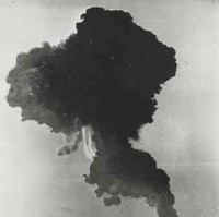 Image: A large mushroom cloud dissipates over a vast, flat expanse of land. A line of telephone poles are visible in the foreground