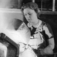 Image: A young woman welds a large metal bracket held in a vise