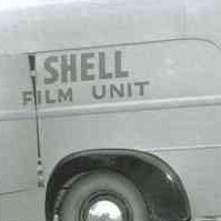 Image: A man in 1950s attire loads equipment into a panel van. The words ‘Shell Film Unit’ are painted on the side and back of the van