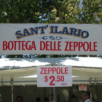 Image: A group of people patronise a food concession housed in a white tent. A sign in Italian on the tent reads “Sant’ Ilario, Bottega Delle Zeppole”