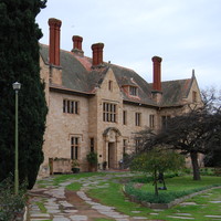 Image: Oblique view of the front of a large, two-storey stone mansion flanked by gardens