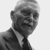 Image: A photographic portrait of a moustachioed middle-aged man wearing a suit
