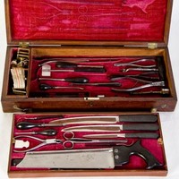 Image: Red velvet lined wooden box containing various 19th century medical instruments including forceps, knives and a saw 