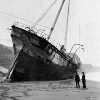Image: A large sailing ship sits stranded on the beach, two men stand observing from the side