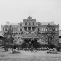 Image: Front view of a historic building with a small garden and trees at the front