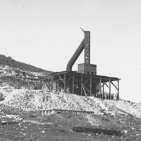 Image: A large chimney mounted on a wooden platform on the side of a hill. Several men stand at the base of the platform