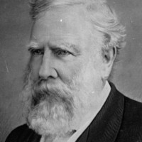 Image: A head-and-shoulders profile of a middle-aged man with white hair and beard. The man is wearing late-Victorian attire