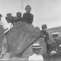 Black and white photo of group of people around engraved rock. 