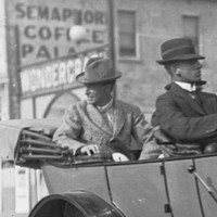 Image: Four men travel in an early twentieth-century car. A couple of buildings are visible in the background, including one with the words ‘Semaphore Coffee Palace’ painted on its side
