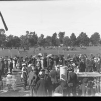 Image: A large group of people gathered on an oval with farm machinery on exhibition.
