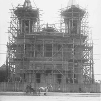 Image: A large stone church with twin spires is under construction and surrounded by scaffolding