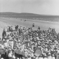 Image: Large group of children wearing hats on a beach with hills in the background