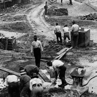Image: a large demolition site with piles of rubble. The site is dotted with men in early 20th century clothing and horse drawn carts. 