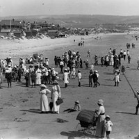 Image: People on a beach with houses and hills in the background.