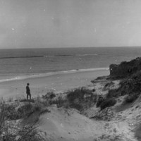 Image: Man on a beach with sand dunes in the foreground.