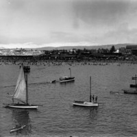 Image: View of boats in the water with crowds of people on the beach in the background