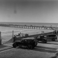 Image: View of jetty and beach with automobiles in the foreground in a parking lot.
