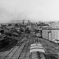 Image: a view of a busy railway yard with a number of parked carriages on a series of tracks. In the background are a series of curved roof buildings.