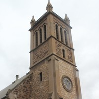 Image: the front entrance of a stone church with a single square tower with a clock. 