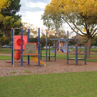 Image: Playground equipment sits in the middle of an open park interspersed with trees of different species