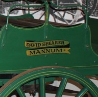 Image: A green automobile with a steam engine and spoked wagon wheels on display in a museum