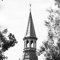 Image: A tower roof with finial and decorative stone arches.