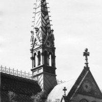 Image: a square gothic style open tower with a very steeply pitched roof rises from the centre of a crossed gable roof
