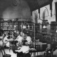 Image: male and female students sit at tables in a library with a vaulted ceiling 
