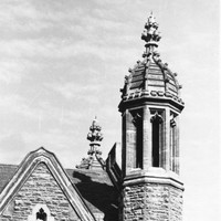 Image: a stone tower with a decorative domed roof rises above a simpler pitched slate roof.