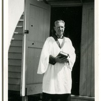 Image: man in robes standing in front of curved tin building
