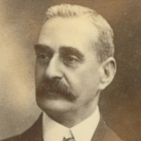 Image: Portrait photograph of a man in an oval frame wearing a suit and tie. 