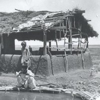 Image: Three men crouch near a pool next to a small, thatch-roofed structure in a remote area