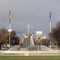 Image: a large fountain made of granite and aluminium featuring seated figures with birds and flanked by two flagpoles flying the Australian and Indigenous flags. 