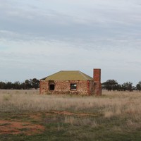 Image: Colour photo of an abandoned brick building in a field.