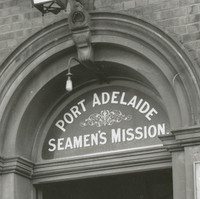 Image: Four Caucasian men in early twentieth century attire stand outside the front entrance of a large bluestone building. A sign above the entrance door reads ‘Port Adelaide Seamen’s Mission’  