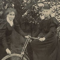Image: a woman sitting astride a bicycle, with two younger women alongside