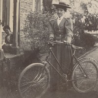 Image: a woman standing beside a bicycle at the side of a stone building