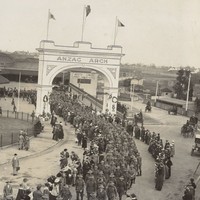 Image: Large group of men in uniform walking through arch and along path