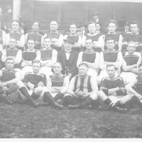 Image: A uniformed sports team poses for a photograph. A man in suit and hat sits in the centre of the group