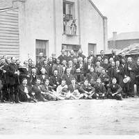 Image: Black and white photograph of men at rear exterior of a building