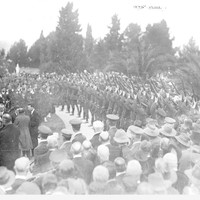 Image: large group of people, men in uniform lined up with guns pointing to the air. 