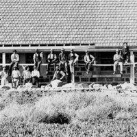 Image: A group of Caucasian workmen in early Edwardian attire sit on scaffolding in front of a long stone building. The building is divided into three separate dwellings with verandahs