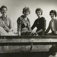 Image: Four smiling women seated on a metal object