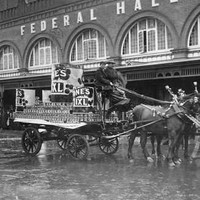 Image: A horse-drawn cart passes in front of a large brick building with the words ‘Federal Hall’ in large letters on its front facade