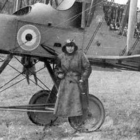 Image: A man in a First World War-era flying outfit stands in front of a British Royal Air Force biplane